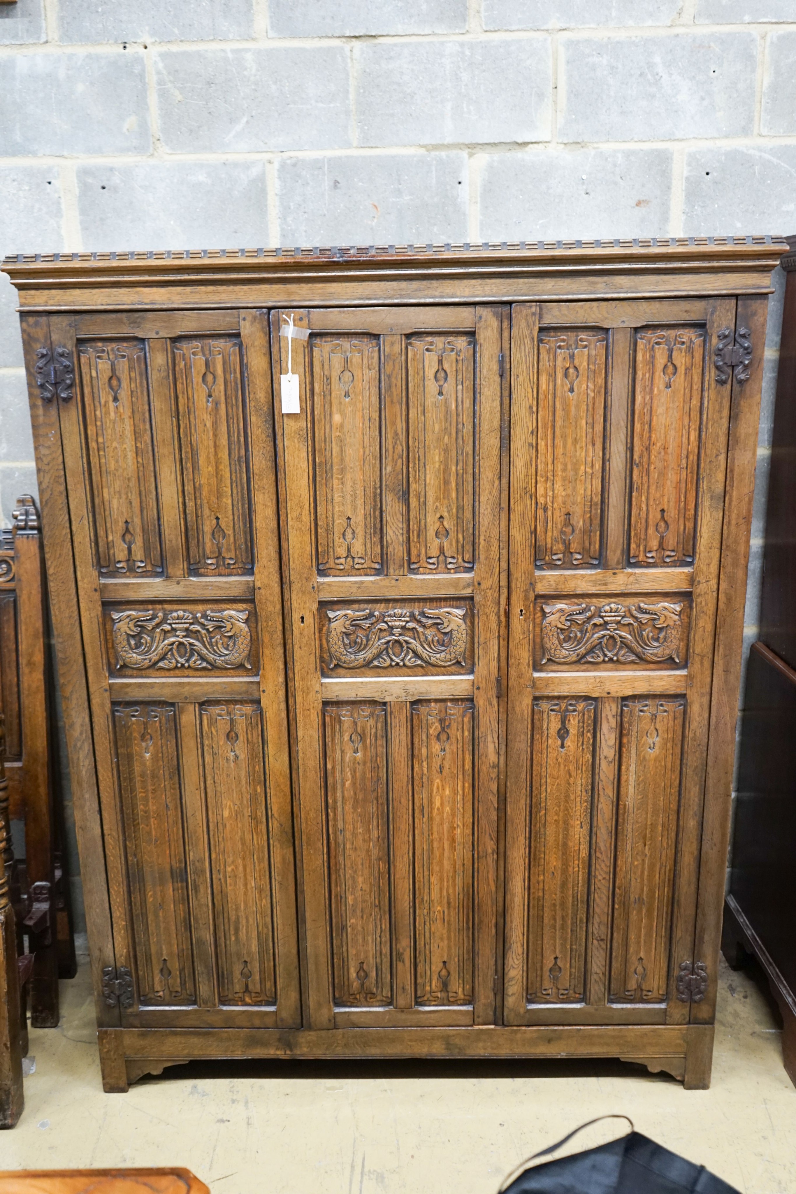 A 17th century style carved and panelled oak triple wardrobe with linenfold decoration, and a pair of early 20th century revival linenfold carved single bedframes, width 91cm, height 130cm